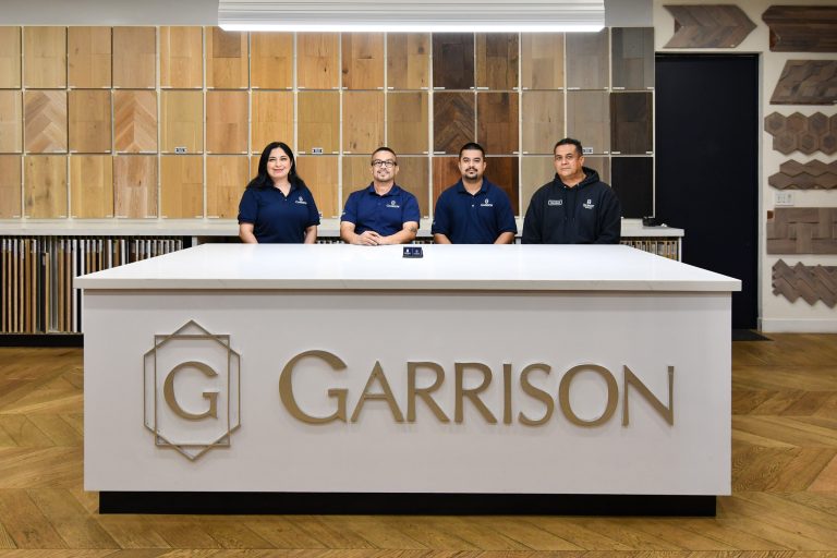 A team of Garrison flooring sales representative standing behind a table with flooring samples on the wall